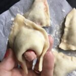 (This is actually a fried cherry pie shaped like a wonton but a good example of this step in the wonton fold) - Bring the wonton around your finger to create and indention and then cross one of the hanging "flaps" over the other, dab a little water or slurry and seal pinching the two flaps together