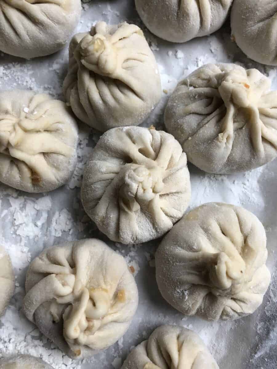 raw homemade xiao long bao sitting on a parchment-lined baking tray