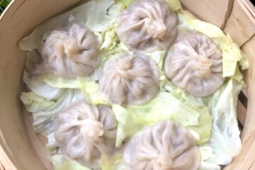 Just steamed xiao long bao soup dumplings sitting atop cabbage leaves in a bamboo steamer