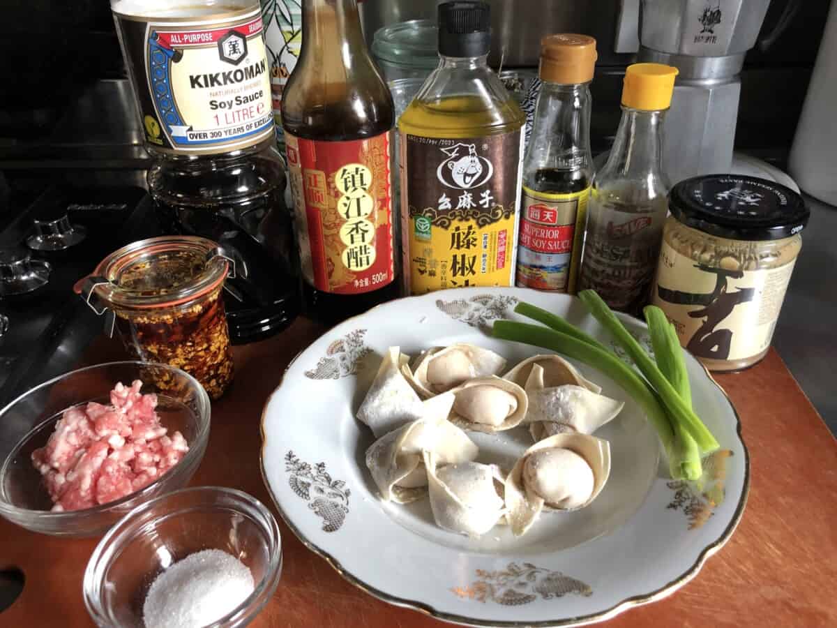 sichuan wonton ingredients on a cutting board with the filled wontons and ground pork and all the seasoning ingredients