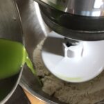 adding green spinach water to the bao bun ingredients in a stand mixer