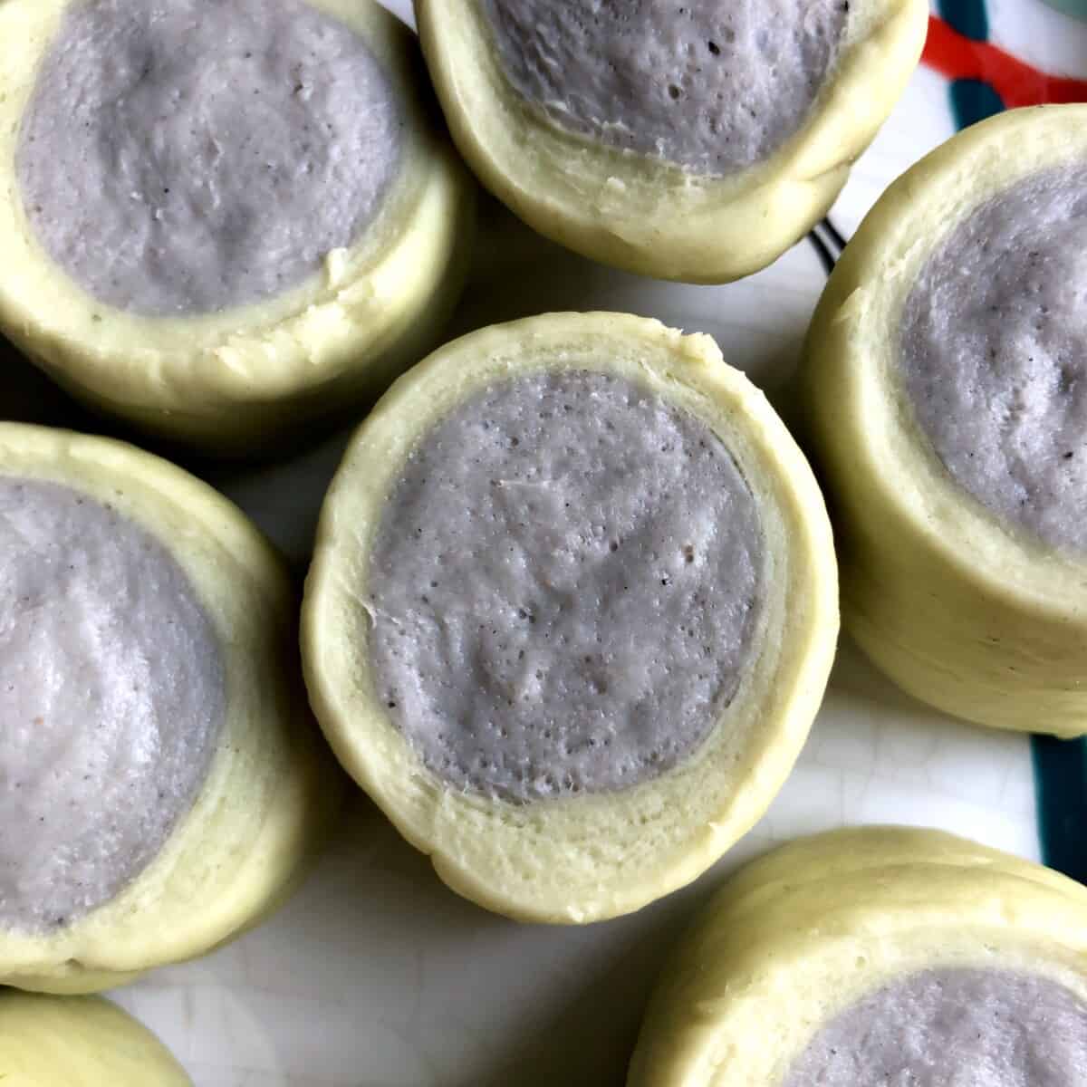 Homemade tie-dyed pork bun dough with a grey center surrounded by a pale green outer perimeter (just after being sliced from the "log" of dough and not yet formed or rolled out.