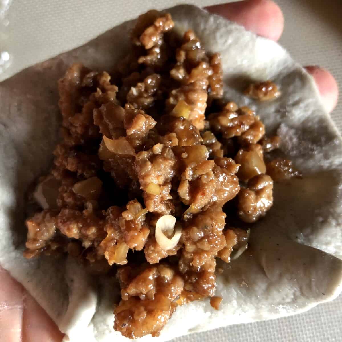 meat filling inside a rolled out bao dough wrapper