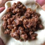a mound of pork filling mixture in a bao bun wrapper that needs to be sealed up