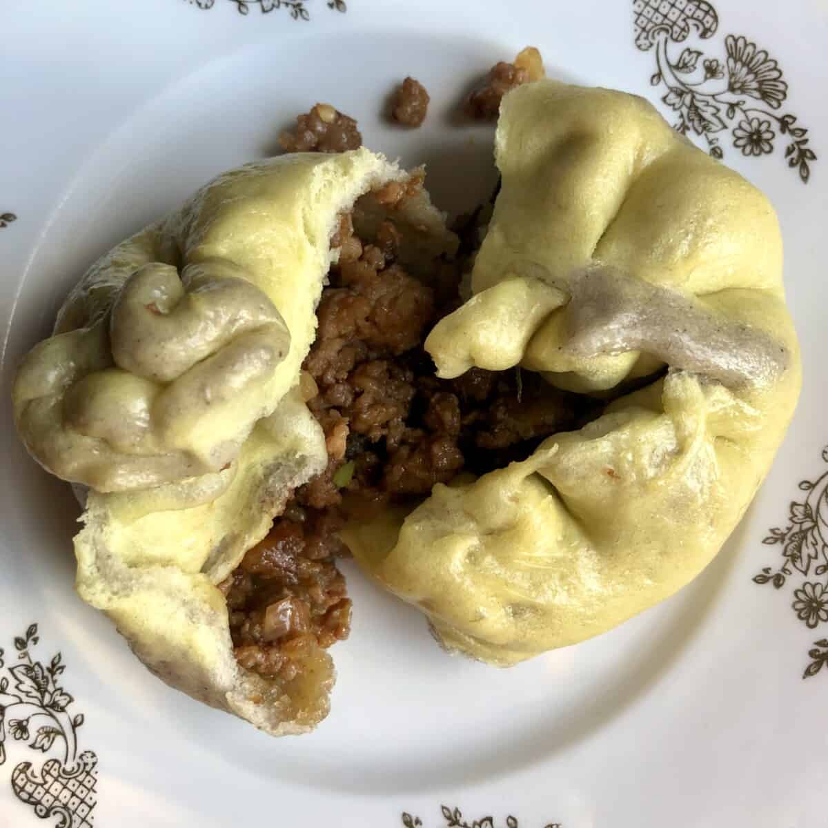 Chinese baozi pork and chicken bun after breaking it open (green and grey tie dyed bun dough wrapped around a pork and chicken filling)