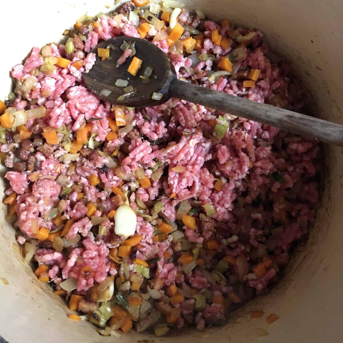 the beef has been added to the pot with a wooden spoon starting to break it up