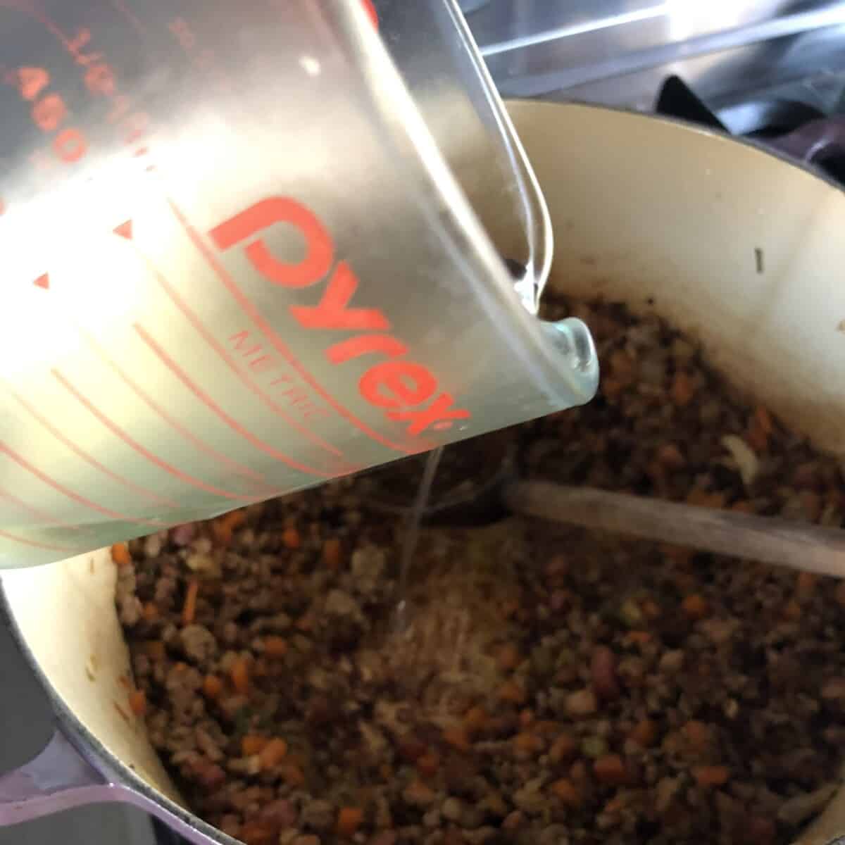 pouring white wine into the Le Creuset dutch oven