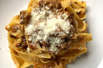a pasta bowl full of papperdelle alla Bolognese sprinkled with Grana Padano cheese