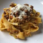 Pappardelle alla Bolognese serving sprinkled with grated Parmigiano-Reggiano cheese