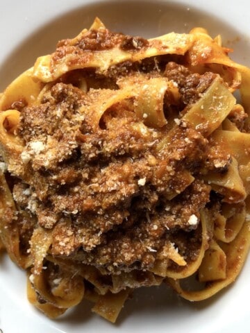 A bowl of traditional pappardelle pasta with rich Bolognese ragù sauce, garnished with freshly grated Parmigiano-Reggiano cheese