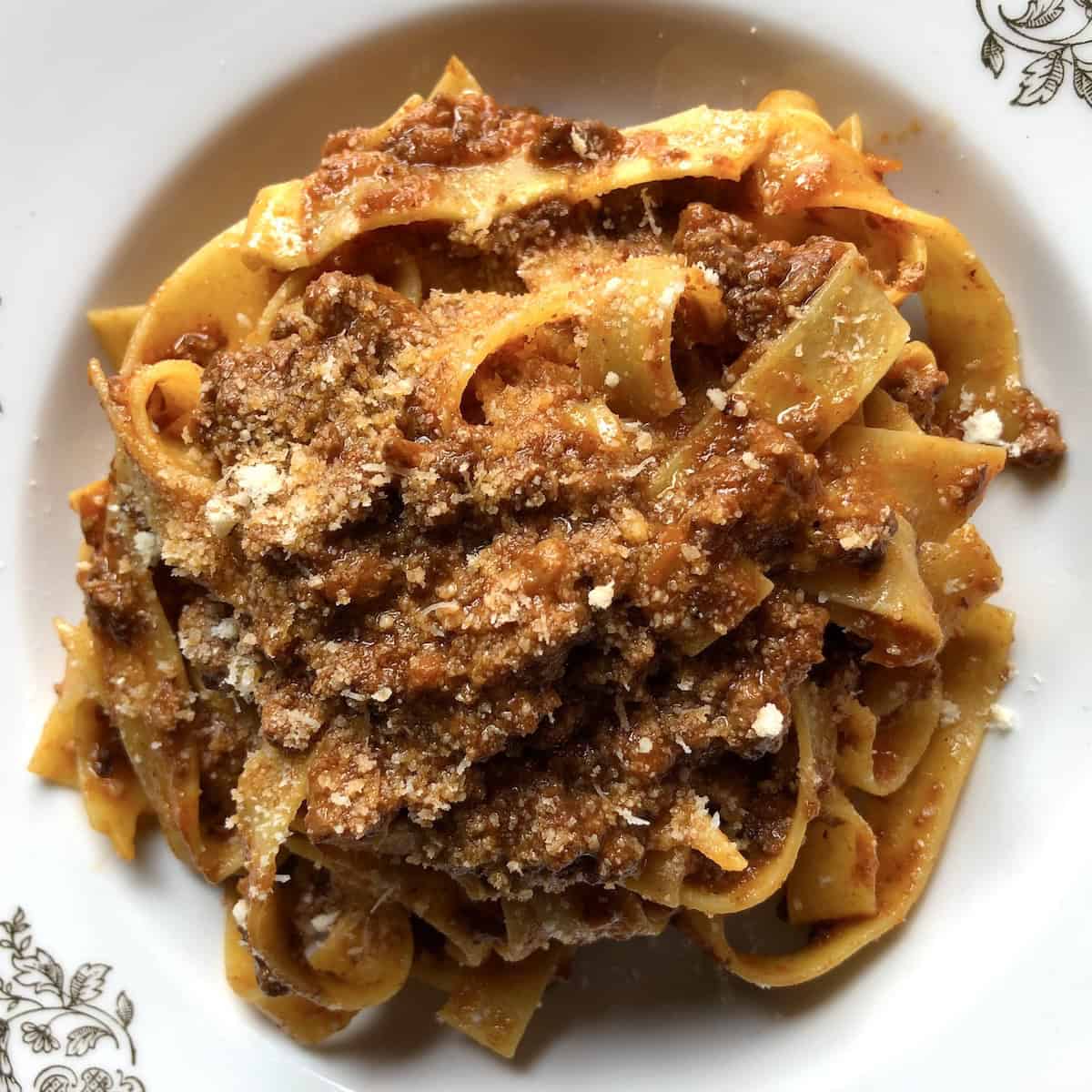 A bowl of traditional pappardelle pasta with rich Bolognese ragù sauce, garnished with freshly grated Parmigiano-Reggiano cheese