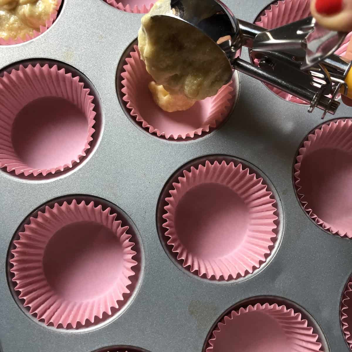Using a portion scoop to add chocolate chip banana bread batter into a lined muffin tin, one bowl banana bread muffin method.