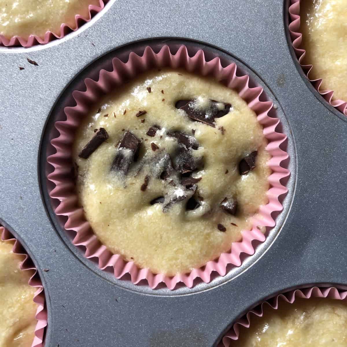 Closeup of a chocolate chip banana bread muffin with chocolate chunks mostly submerged into the batter and ready to bake.