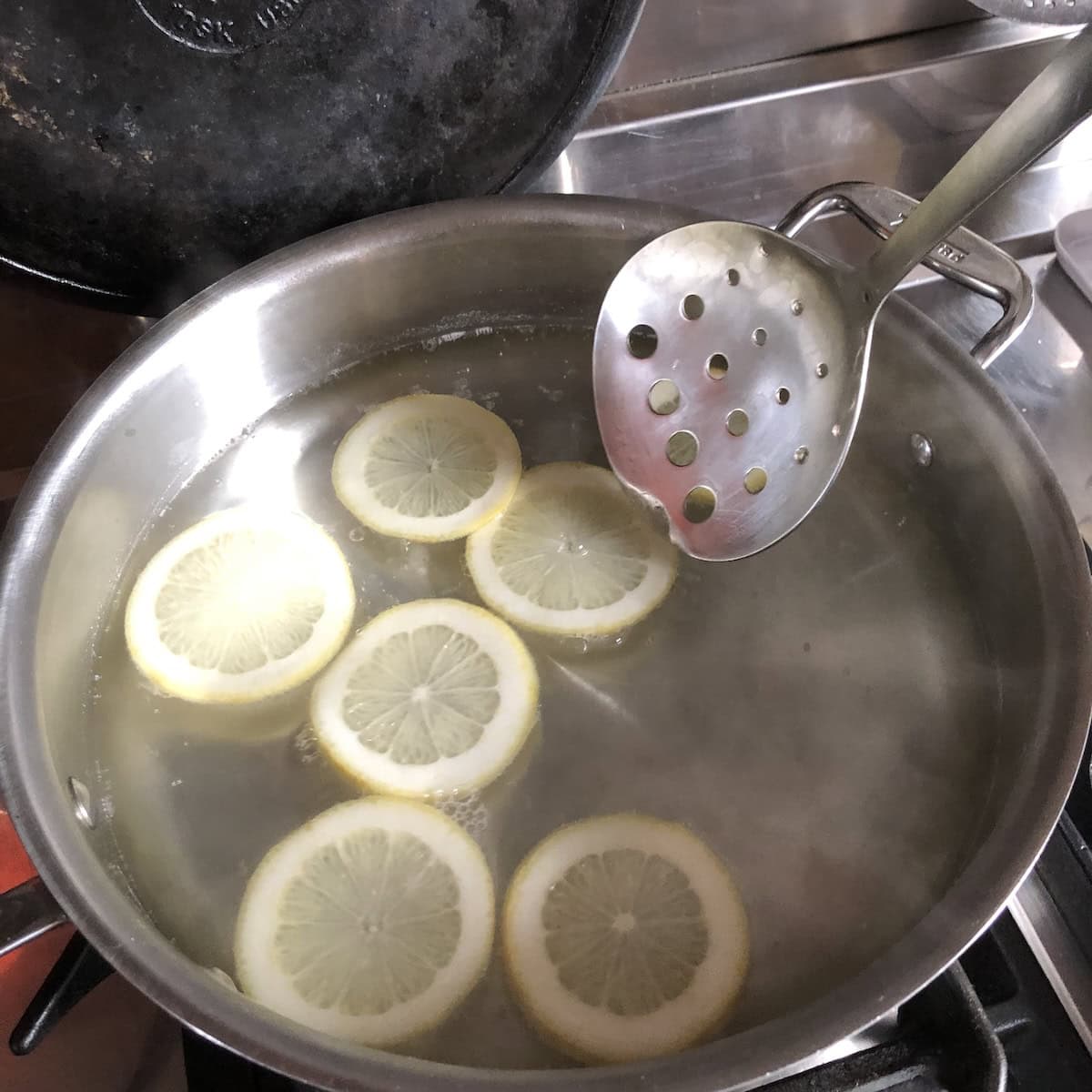 Cooking lemon slices in simple syrup to candy them, repurposing leftover peeled lemons from a homemade limoncello recipe into candied lemon treats.
