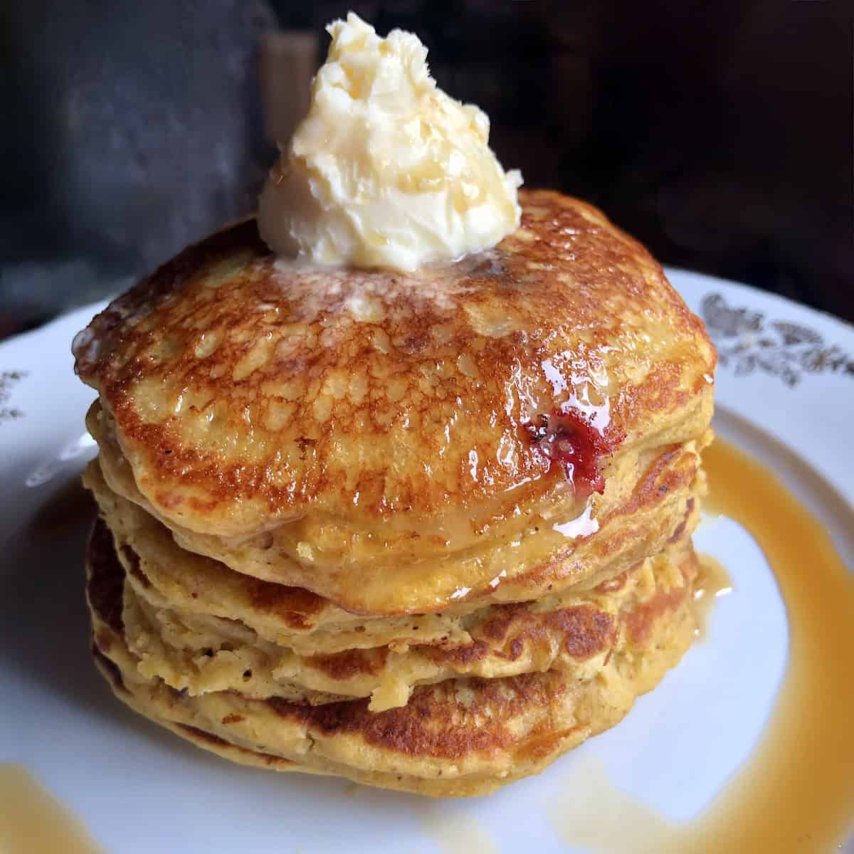 A steaming hot pile of glistening, golden brown pumpkin pancakes filled with berries and toasted pecans and topped with a knob of butter and pure maple syrup.