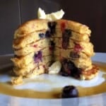 Stack of fluffy pumpkin pancakes with mixed berries showing a wedge removed revealing the fluffy interior.