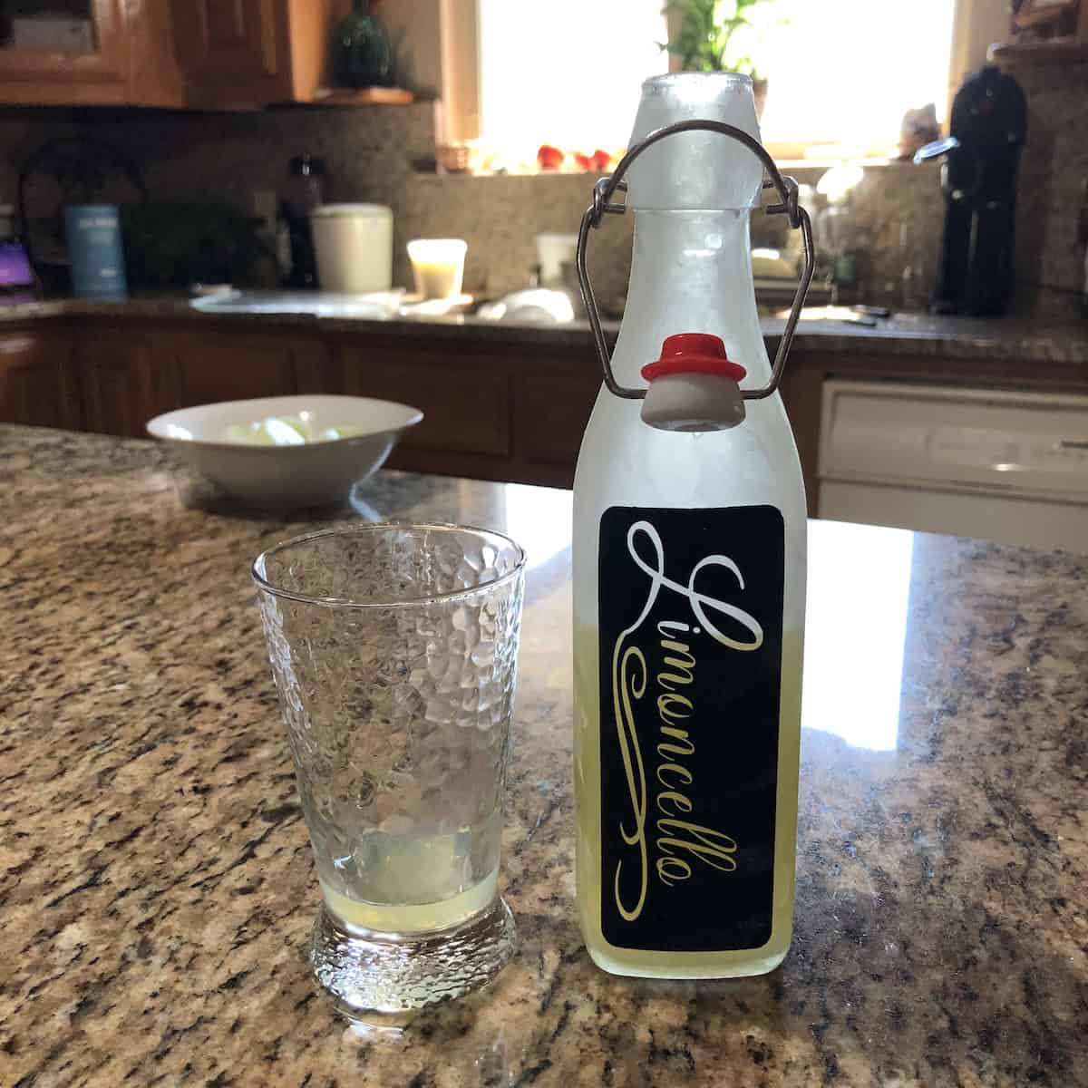 Homemade limoncello in a swing top bottle with a custom black label and the word limoncello cut out to show the bright yellow Italian limoncello through the label, homemade limoncello recipe made from scratch.
