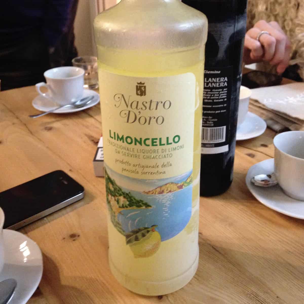 Nonno Franco's homemade limoncello recipe in a repurposed Nastro D'oro bottle surrounded by espresso mugs after a family Christmas dinner.