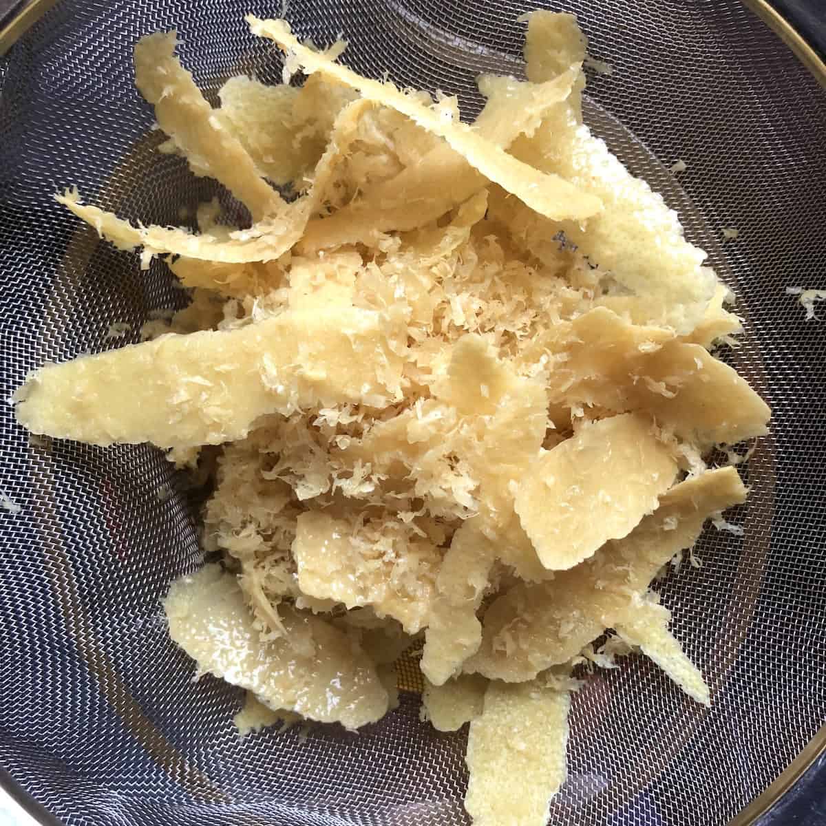 Strained lemon zest and peels in a fine mesh strainer after being separated from the alcohol, brittle and fully cured peels showing the infusion is complete for this best limoncello recipe.

