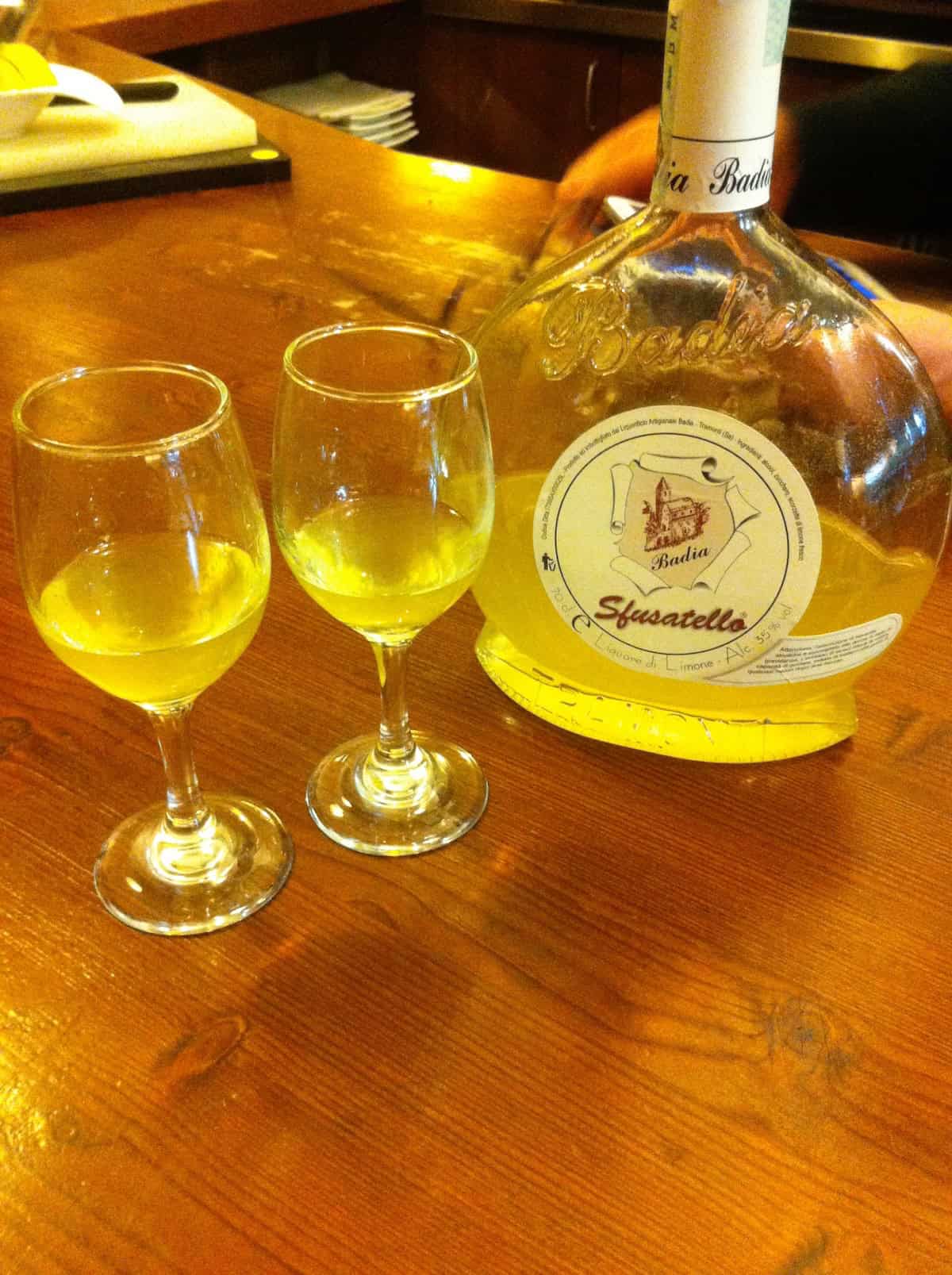 A bottle of Italian Sfusatello limoncello and two glasses served after dinner at a restaurant in the Colli Berici hills, limoncello drinks offered as a customary Italian digestivo.
