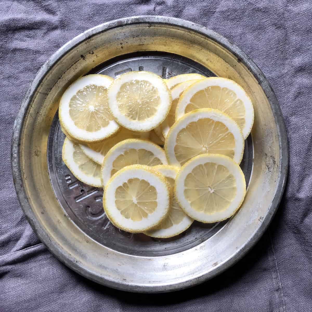 Sliced leftover lemons without zest in a vintage pie tin ready to repurpose into candied lemon peels or homemade lemonade, zero-waste lemon recipes after making homemade limoncello.
