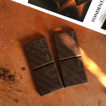 A bar of Lindt 70% Excellence dark chocolate with four squares removed and lying on a cutting board ready to be chopped for chocolate chip banana bread.