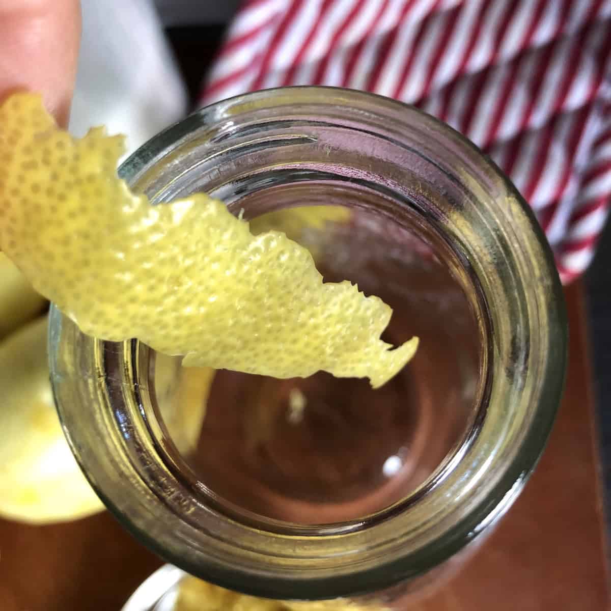 Adding a lemon peel to the jar with alcohol and lemon zest to begin the limoncello infusion, how do you make limoncello with fresh peeled lemon for an Italian limoncello.
