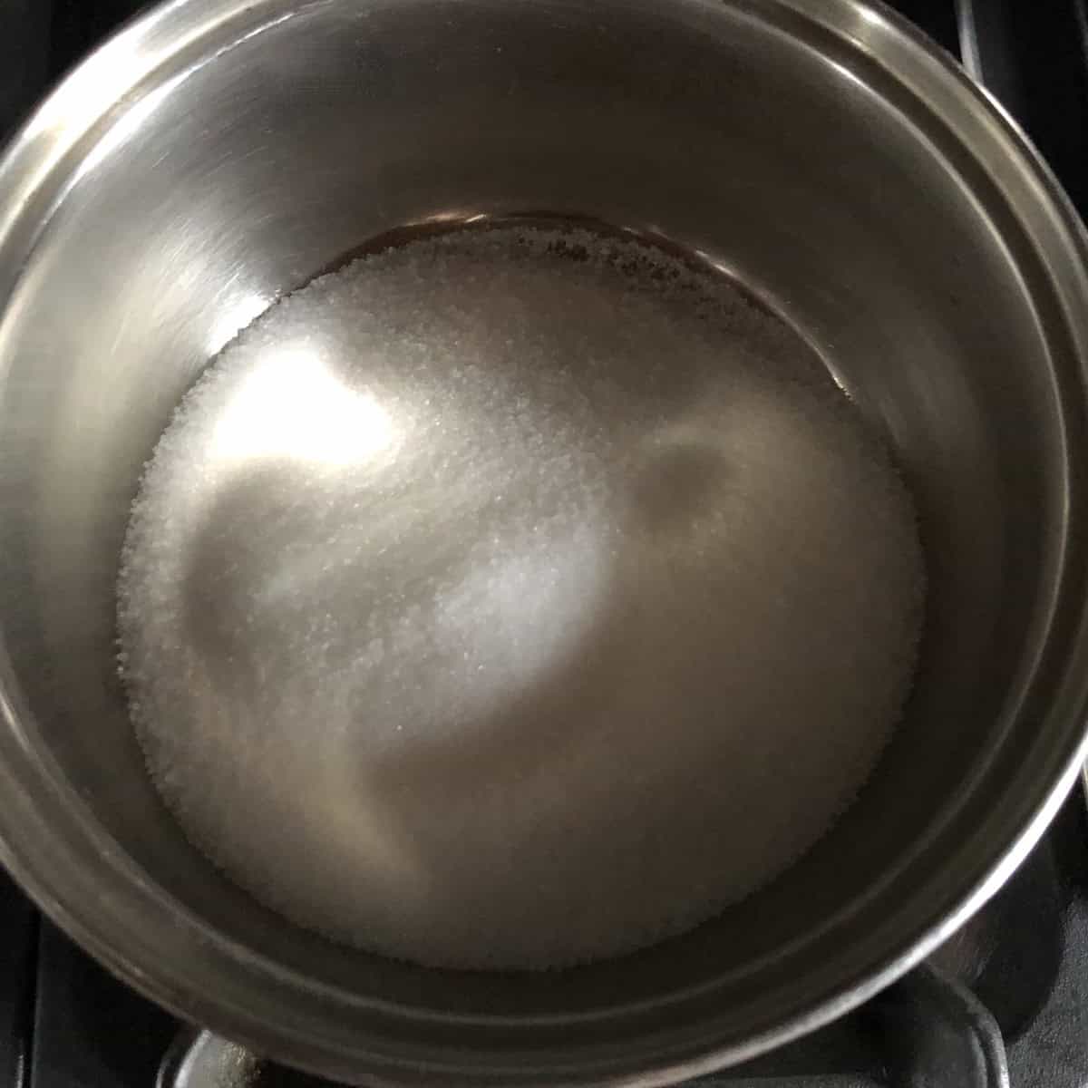 Sugar and water heating over medium heat to make simple syrup for limoncello showing how to sweeten homemade limoncello, recipe for limoncello step by step.
