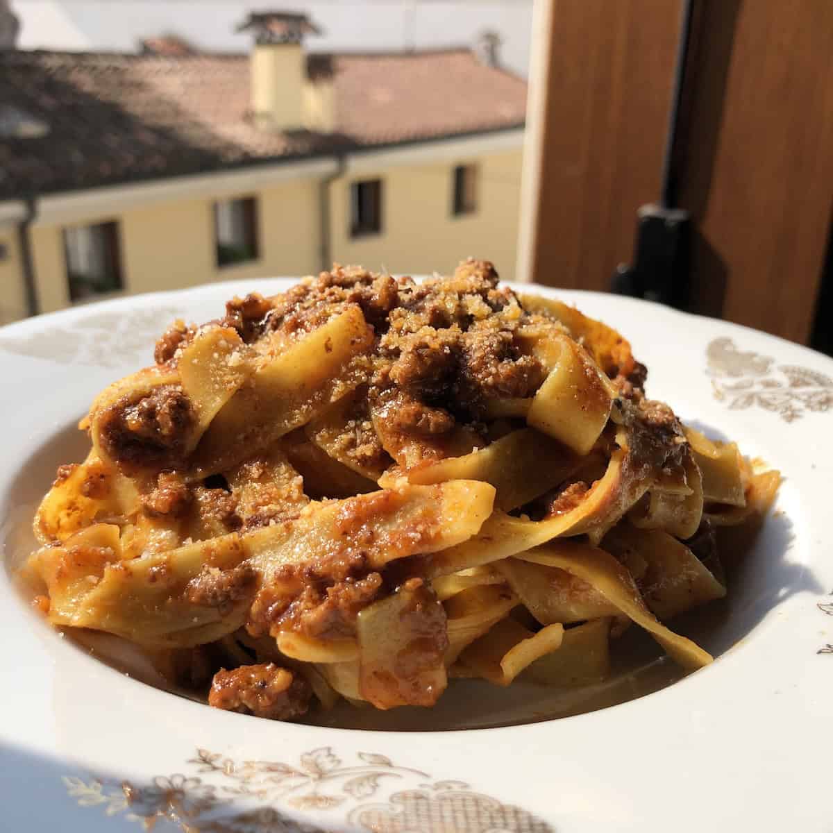 Papparedelle bolognese served in a vintage Italian pasta bowl with a view outside my italian kitchen window in the background.