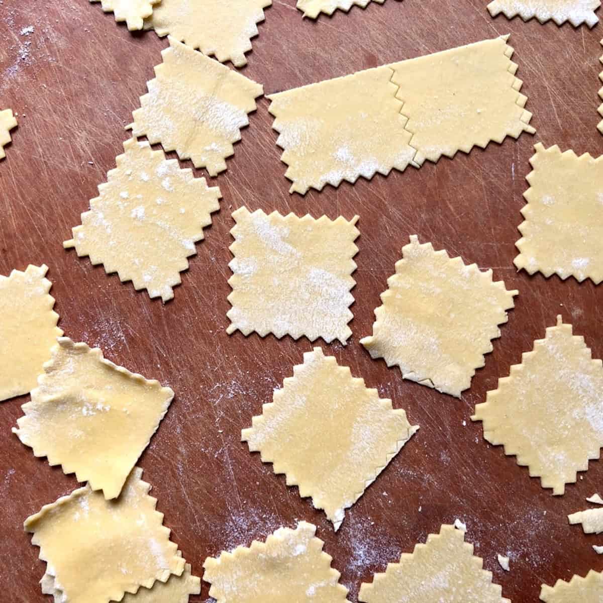 Small squares of 00 flour and semolina pasta dough cut with a reginelle pasta bike for tortellini, pasta dough recipe with semolina and 00 flour rolled and ready to fill.