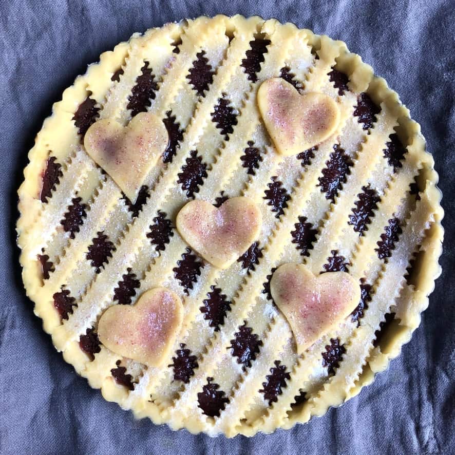 unbaked assembled Italian crostata with diamond lattice with 5 hearts sprinkled with pink sugar