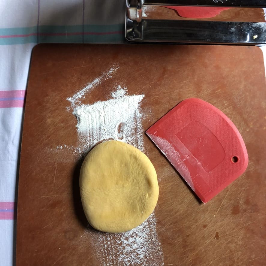 flattened piece of dough on a very lightly floured cutting board about to be rolled