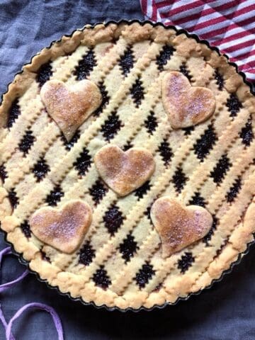 Golden brown crostata di marmellata with lattice top and decorative hearts sprinkled with homemade cherry sugar showing authentic Italian jam tart recipe.