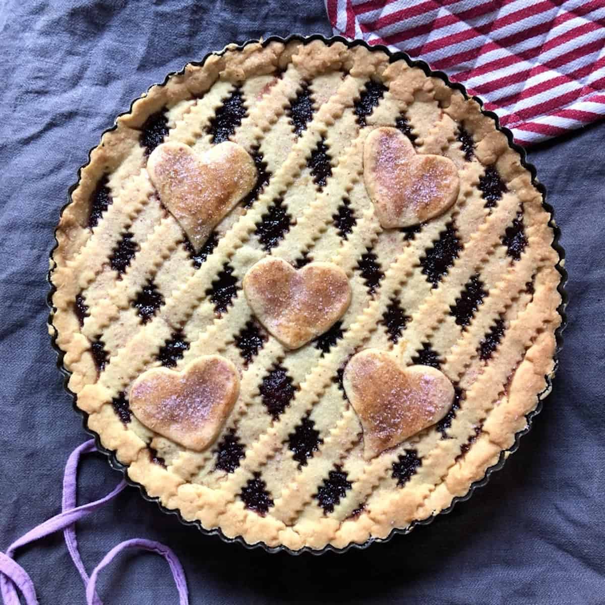 Golden brown crostata di marmellata with lattice top and decorative hearts sprinkled with homemade cherry sugar showing authentic Italian jam tart recipe.