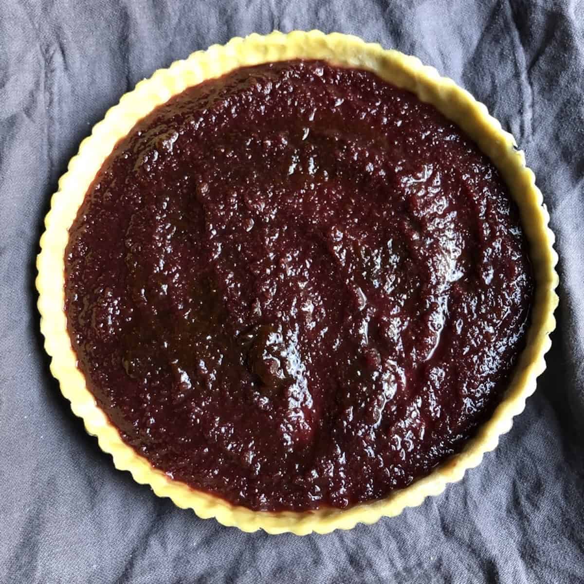 Jam filling spread evenly in pasta frolla crust ready for lattice top and decorative cutouts, showing proper amount of marmellata for Italian crostata di marmellata assembly.