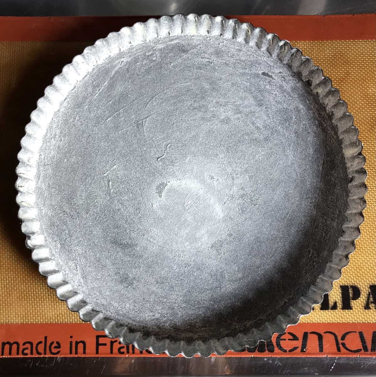 Prepared tart pan evenly coated with flour and excess tapped out, ready for pasta frolla crostata dough, showing properly floured pan for easy Italian jam tart release after baking.