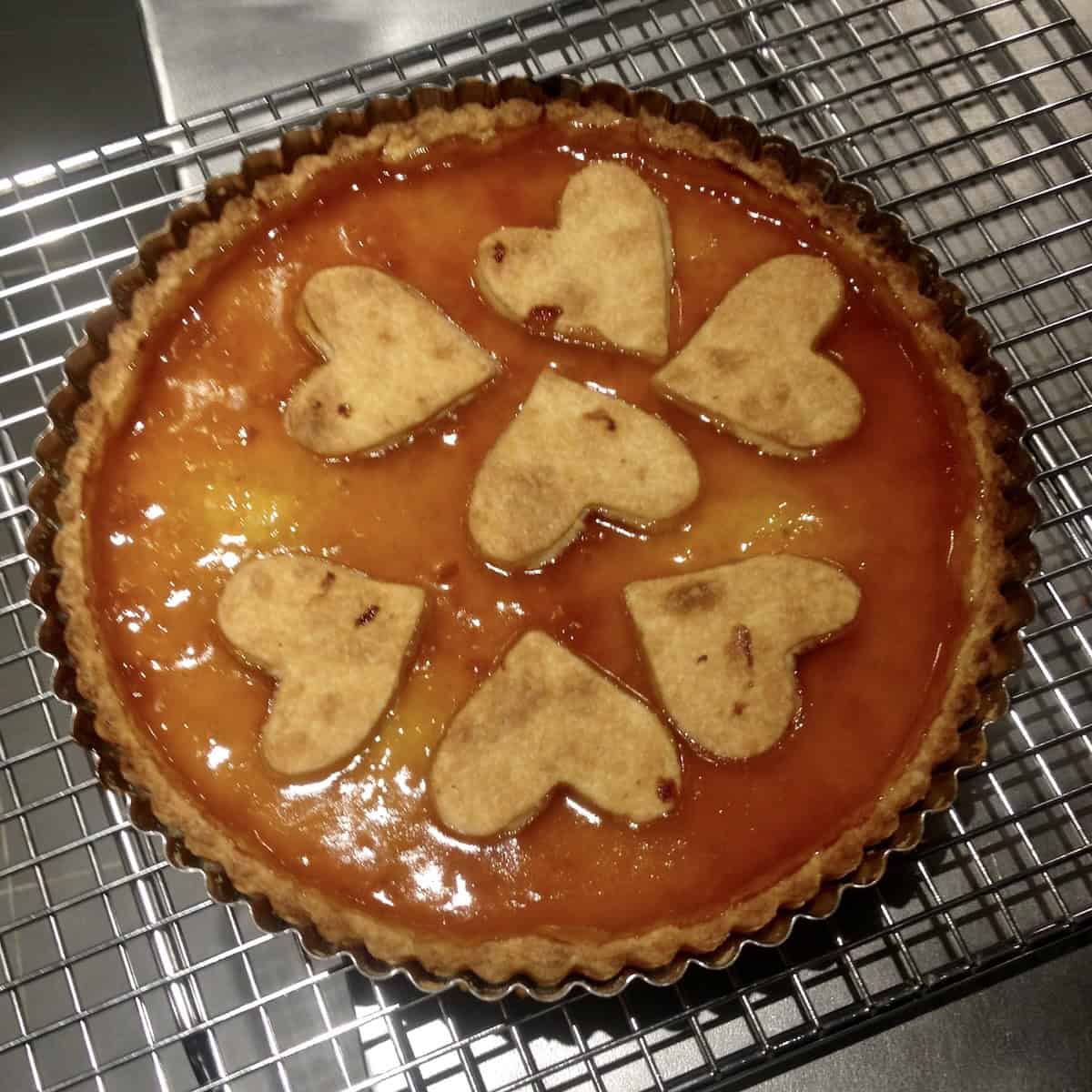 Homemade apricot crostata (crostata all'albicocca) decorated with heart-shaped pasta frolla cutouts on golden lattice top, perfect Italian jam tart for Valentine's Day or romantic dessert with sweet apricot jam filling.