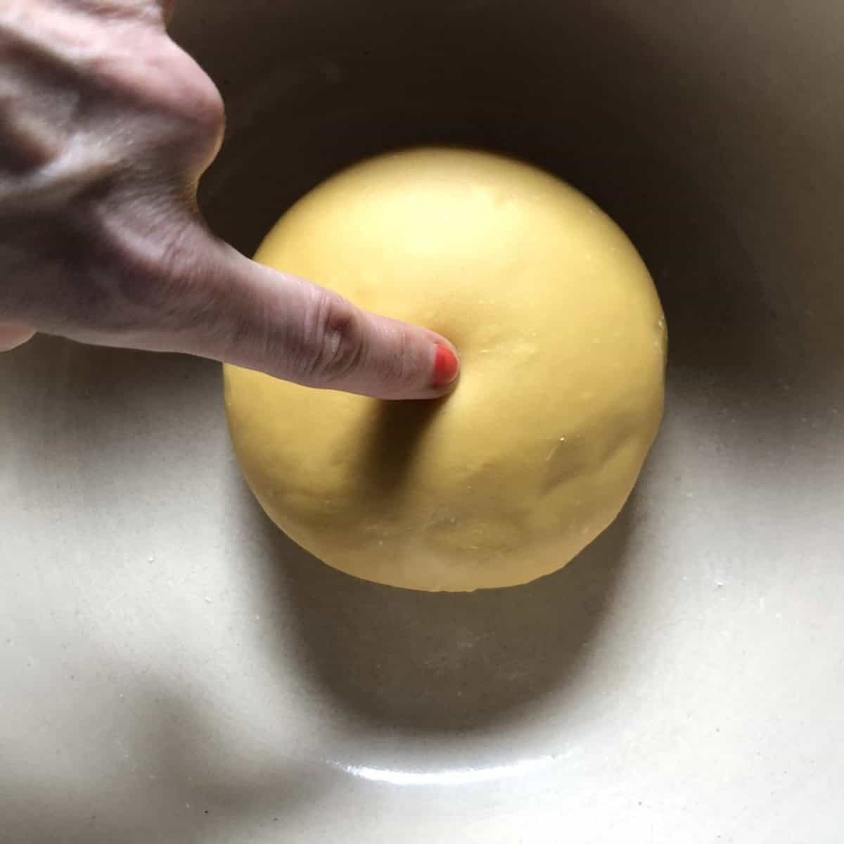 My finger poking the center of the rested semolina and 00 flour pasta dough to test if it is fully relaxed.