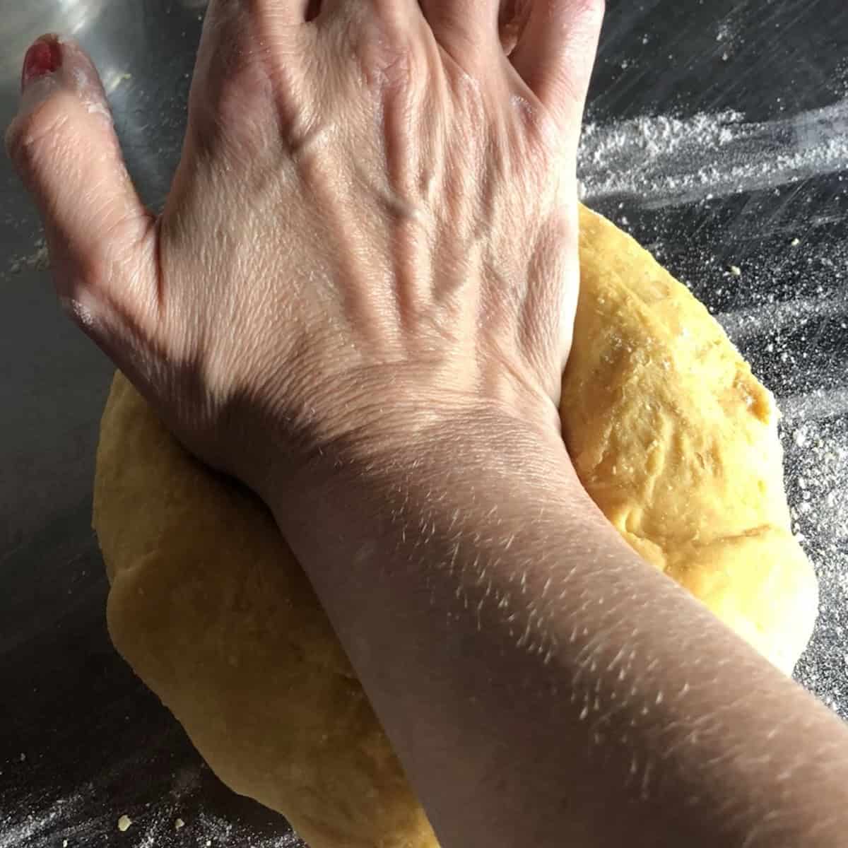 Hand kneading semolina and 00 flour pasta dough on a floured surface, homemade pasta with 00 flour and semolina rimacinata.