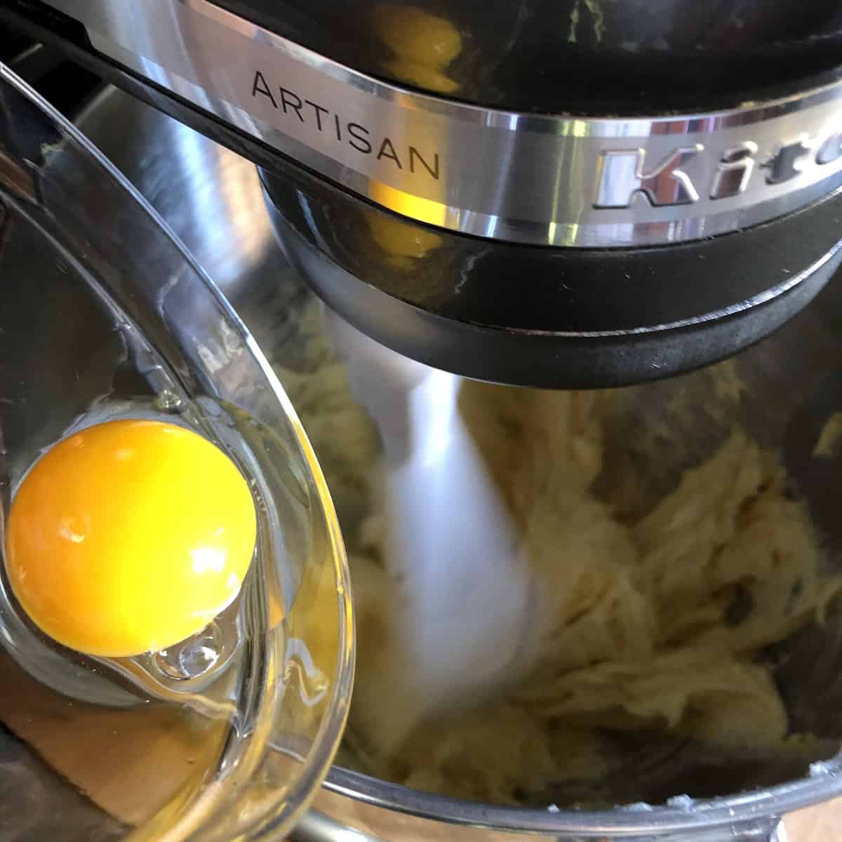 Adding egg and egg yolks one at a time to creamed butter mixture for pasta frolla, incorporating each egg just until combined for tender Italian crostata dough.