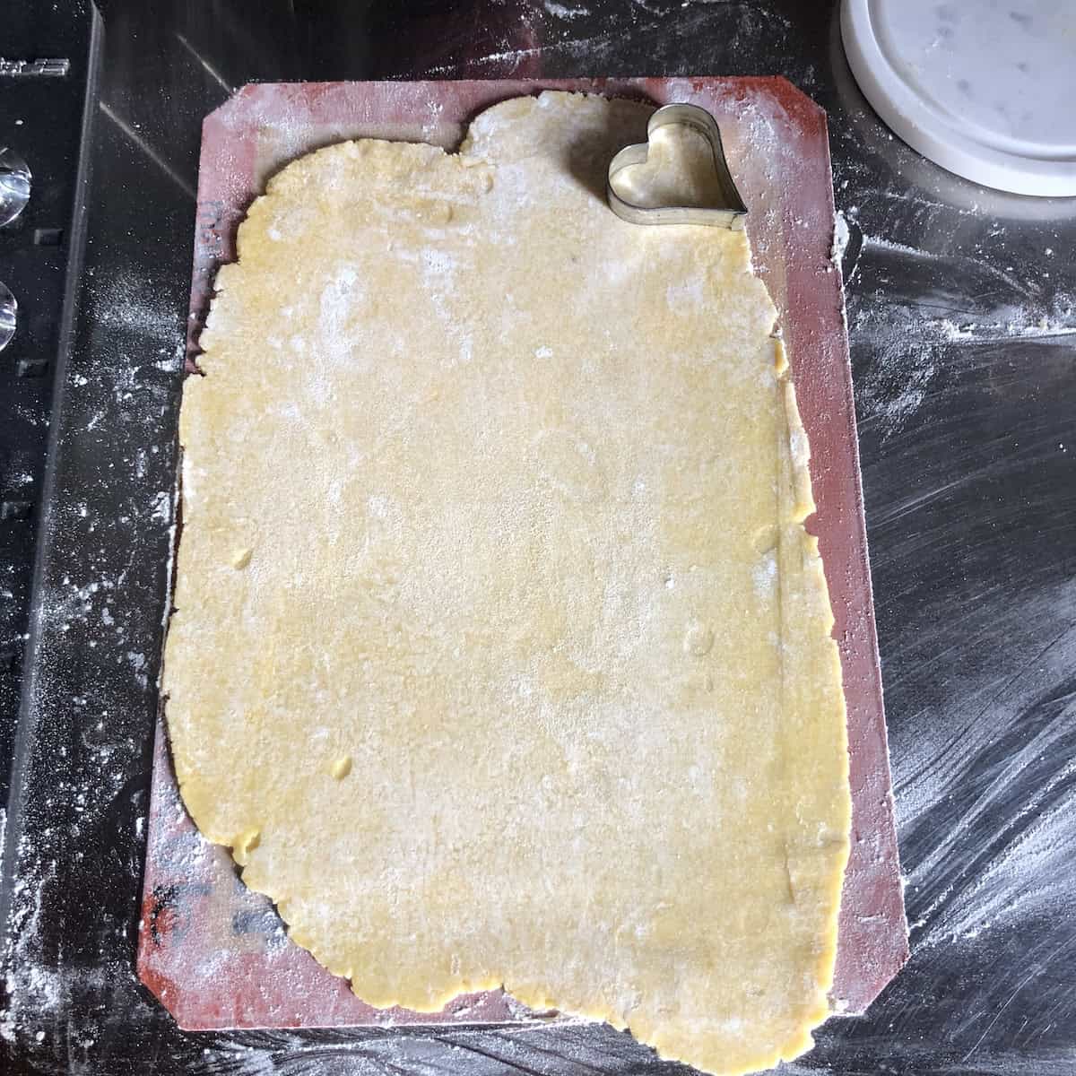 Cutting decorative heart shapes from pasta frolla dough with cookie cutter to decorate crostata lattice top, adding romantic Italian jam tart decoration for Valentine's Day or special occasions like Mother's Day.