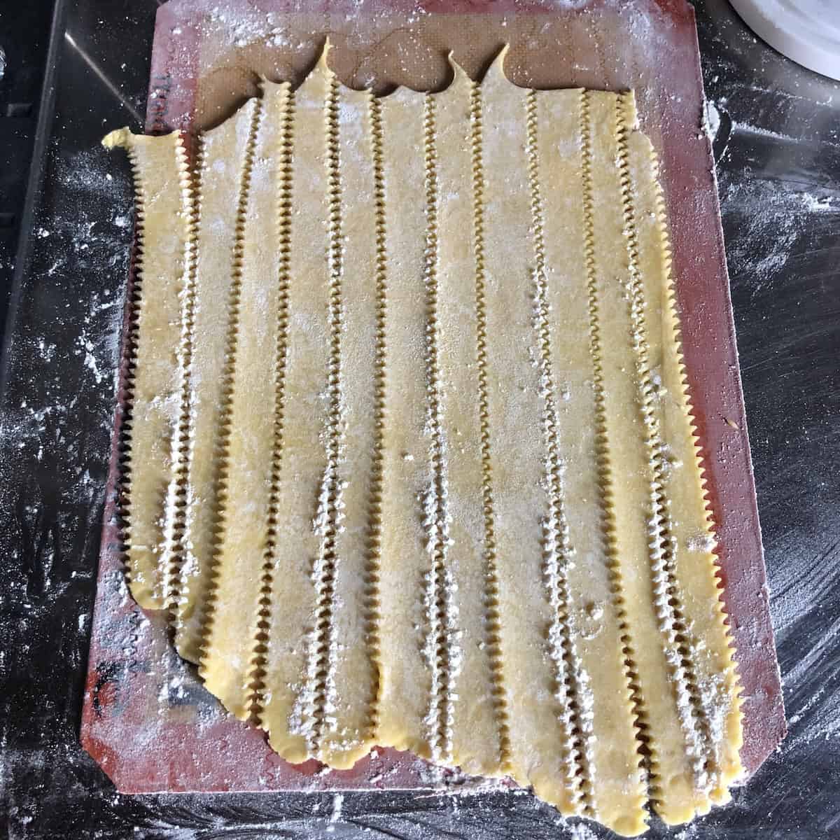 Cutting pasta frolla lattice strips with pasta bike wheel to create traditional reginelle zigzag edges for Italian crostata top, showing how to make authentic lattice-topped jam tart.