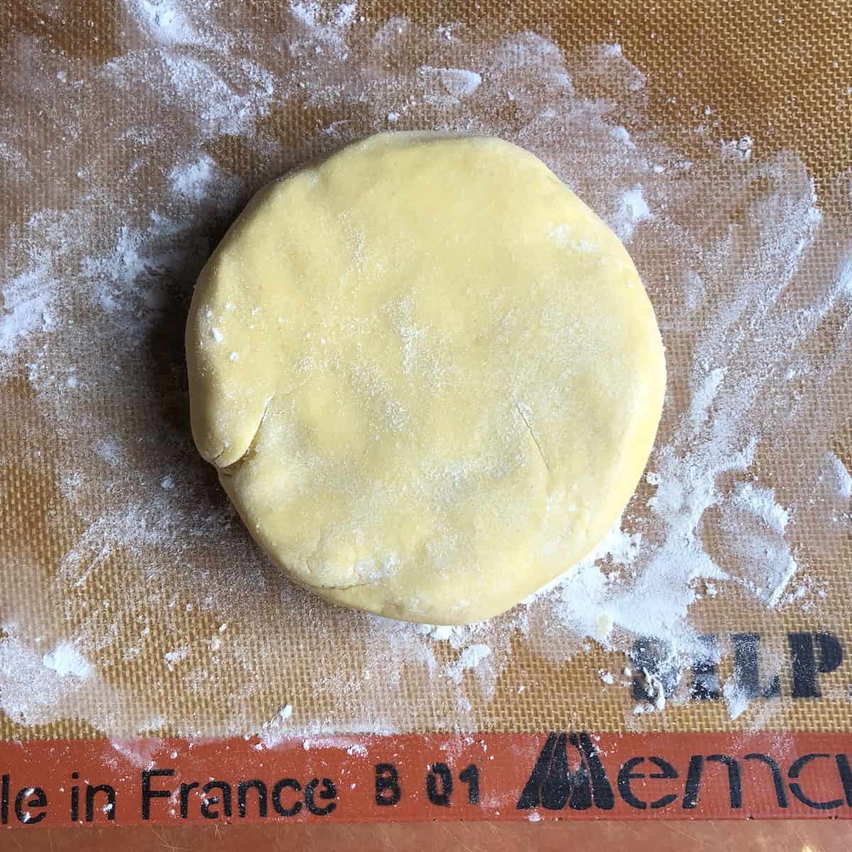 Perfectly formed pasta frolla dough disc ready to be wrapped and refrigerated, showing smooth round shape for Italian crostata shortcrust pastry before chilling for at least 2 hours.