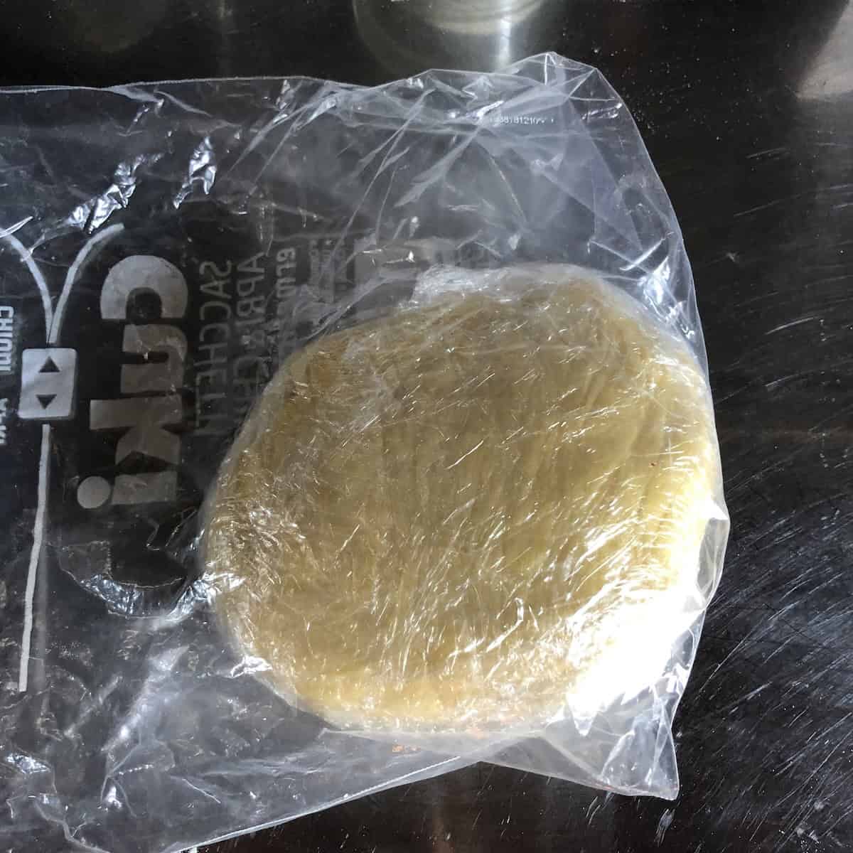 Pasta frolla dough disc wrapped in sustainable cling film and chilled in refrigerator, properly rested Italian crostata dough ready to roll out for jam tart.