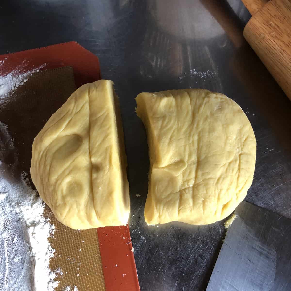 Chilled pasta frolla dough divided into two pieces with one disc slightly larger for the bottom crust, showing how to portion Italian crostata dough for jam tart assembly.
