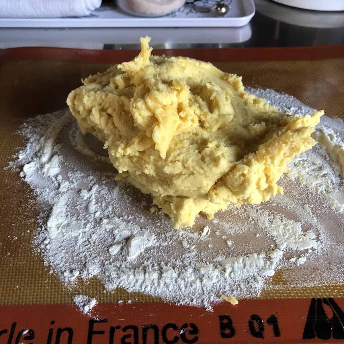 Pasta frolla dough dumped onto lightly floured Silpat mat ready to be gently formed into a disc for chilling, showing soft texture of Italian crostata dough before refrigerating.