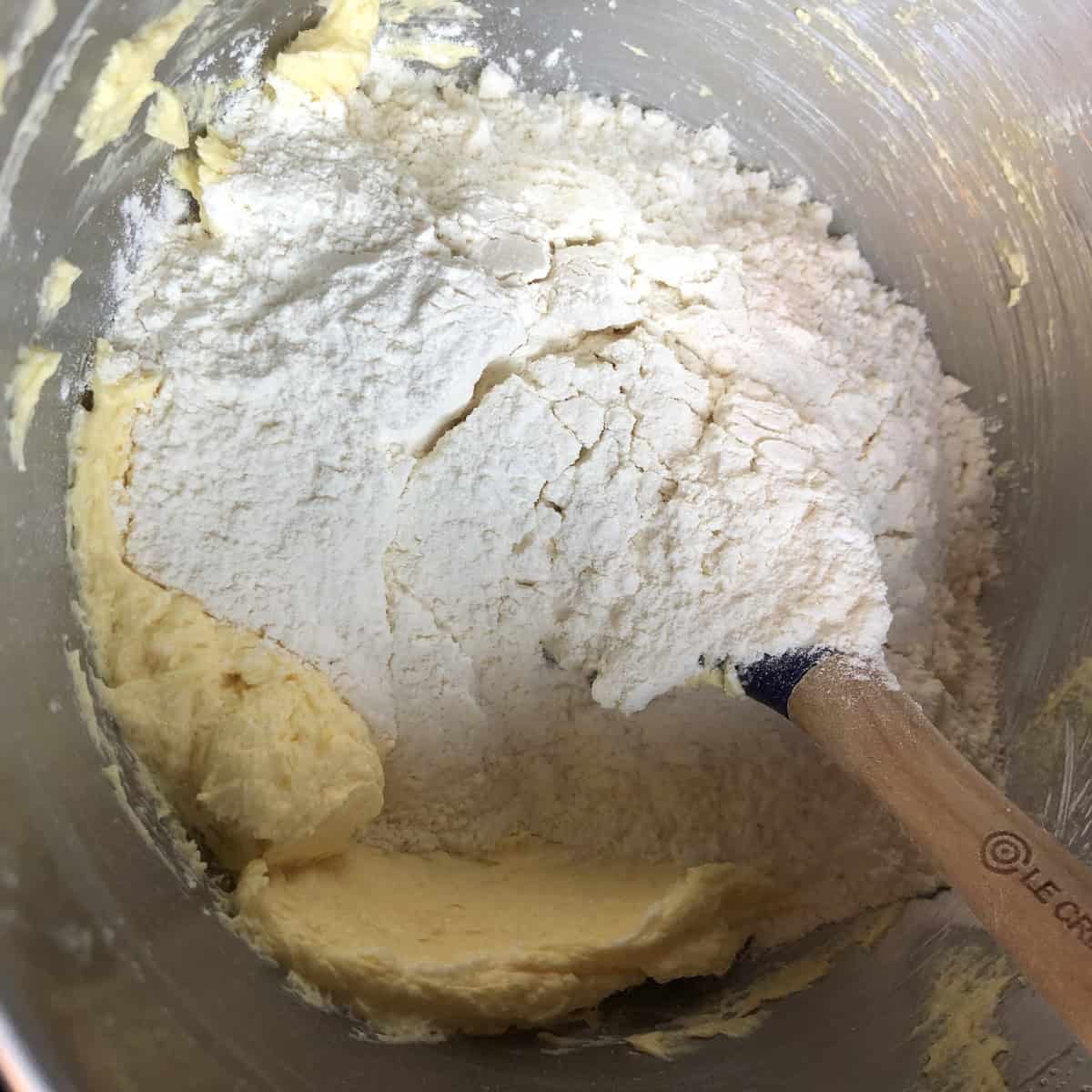 Flour mixture added to creamed butter mixture in stand mixer bowl before being stirred in, showing how to make pasta frolla crostata dough by folding dry ingredients into wet.