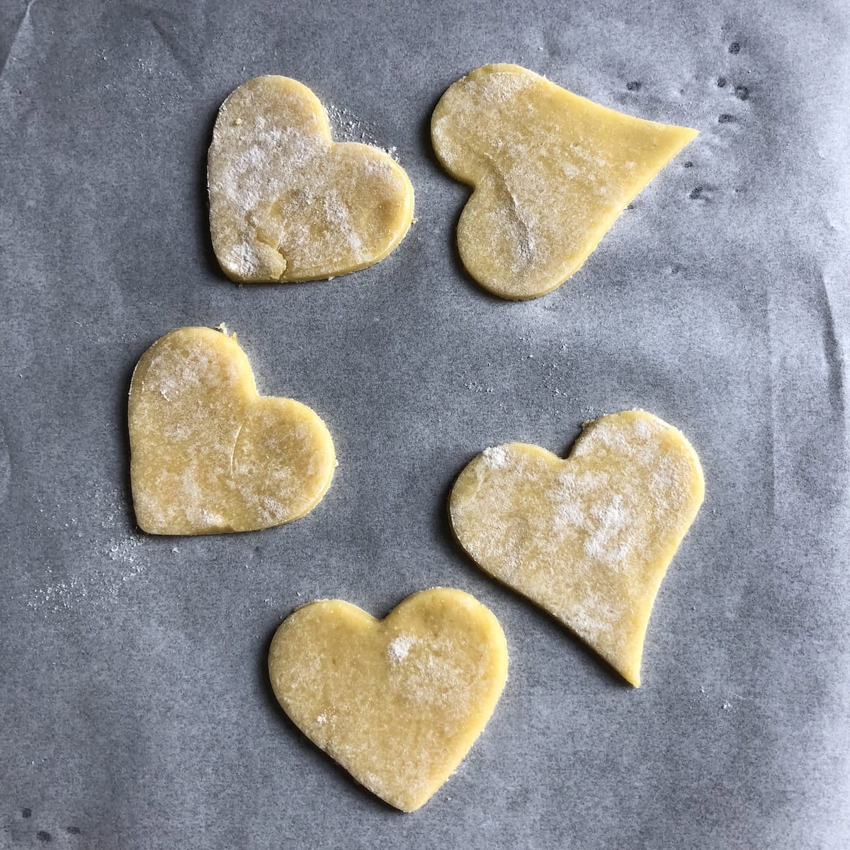 Five pasta frolla heart cutouts ready to decorate crostata for valentines dessert, romantic Italian jam tart topping for Valentine's Day or anniversary celebration.