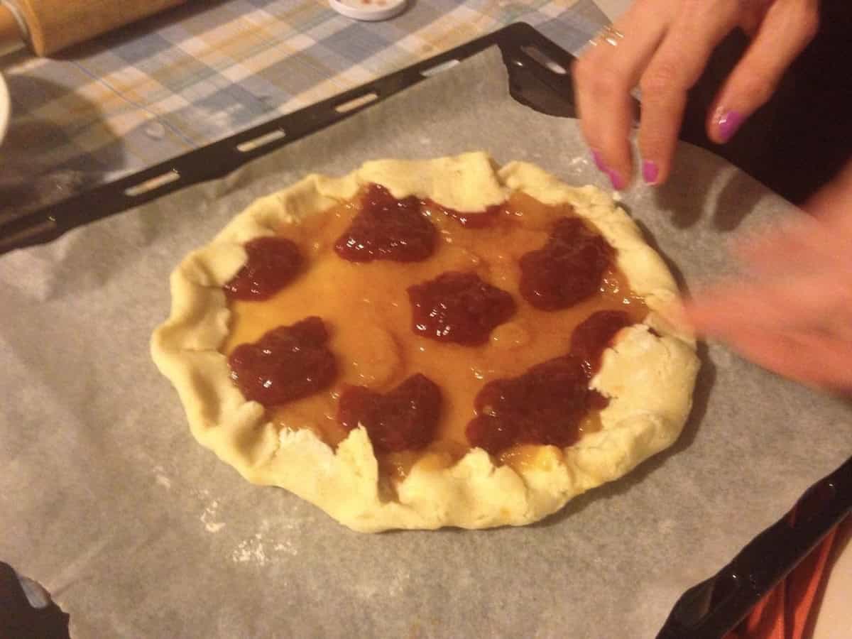 Homemade rustic freeform crostata with apricot and raspberry jam showing what not to do when making Italian jam tart, with too much jam filling that will bubble over and spill during baking, demonstrating common crostata mistake to avoid when folding pasta frolla dough edges over filling without a tart pan.