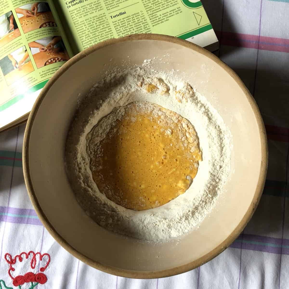 Using a fork to pull the semolina and 00 flour into the creamy yellow egg mixture about halfway combined, pasta dough recipe semolina and 00 flour step by step.